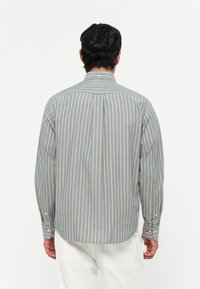 Camicia a righe in azzurro chiaro e giallo, materiale in cotone, maniche lunghe, colletto con bottoni, piega dorsale per facilitare il movimento.