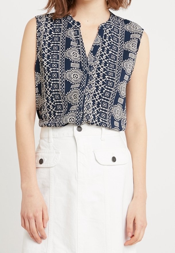 Blouse sans manches bleu marine avec une patte de boutonnage sur le devant, présentant un motif géométrique et cachemire crème. Portée avec une jupe blanche taille haute.