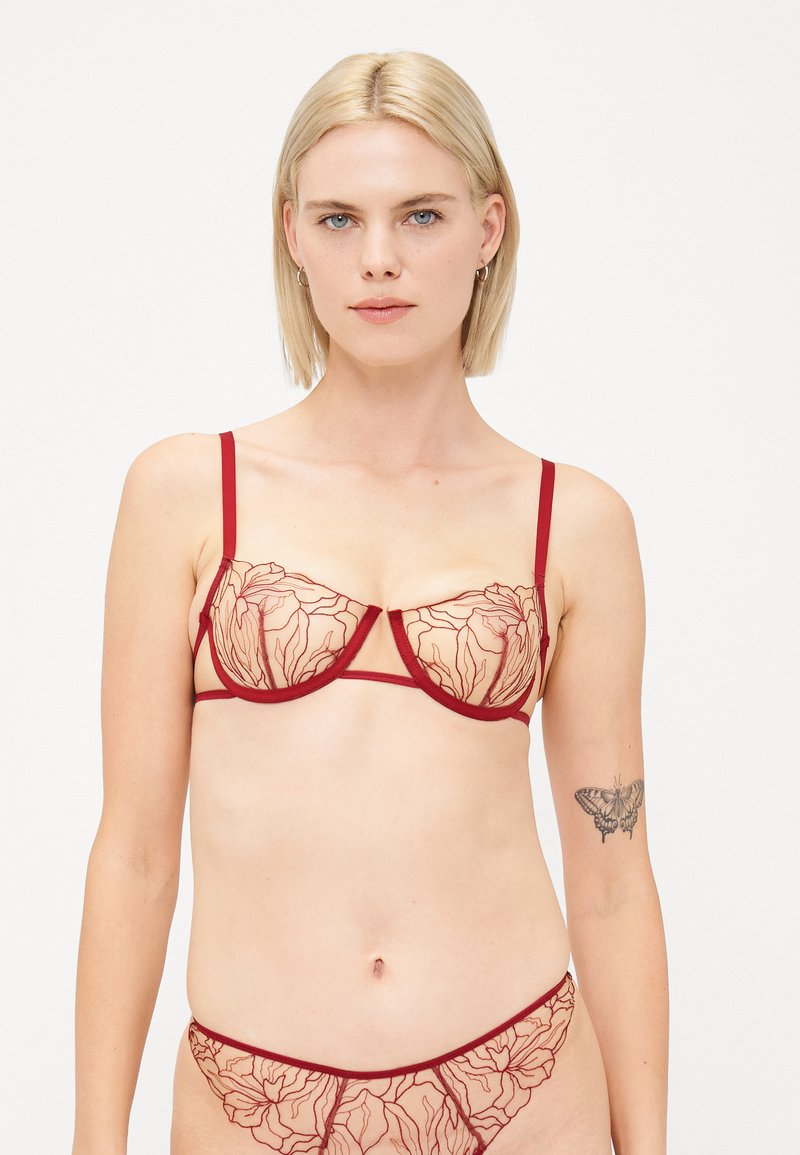 Red bra with sheer floral-patterned cups and thin straps. Matching floral-patterned bikini bottom. Delicate design with contrasting outlines.