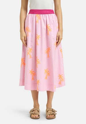 Woman wearing a pink and white striped midi skirt with orange palm tree prints and a pink waistband, paired with beige sandals.