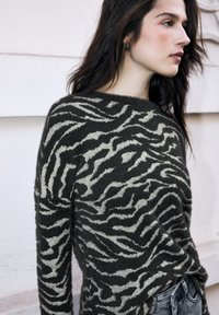 Sweter w paski zebry w ciemnoszarym i kremowym kolorze, wykonany z miękkiej, teksturowanej tkaniny; posiada szeroki dekolt i długie rękawy.