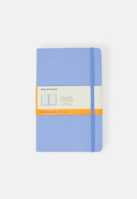 Quaderno Moleskine rilegato in blu chiaro con pagine a righe, tenuto insieme da un elastico blu, con un'etichetta arancione contenente i dettagli del prodotto.