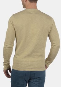 Vaaleanbeige, pitkähihainen paita, jossa pyöreä kaula-aukko, teksturoitua kangasta ja istuvat hihat. Ei näkyviä kuvioita tai yksityiskohtia.