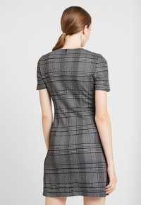 Lyhythihainen mustavalkoinen ruututettu mekko, jossa on istuva malli, lyhyet hihat ja selässä vetoketju. Materiaalissa on teksturoitu pinta.