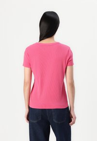 T-shirt rose à manches courtes et à col rond en côtes. Porté avec un jean bleu foncé et ample. Texture lisse, design décontracté.
