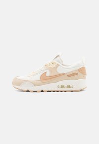 Beige ja valge Nike Air Max nohvik, mille põhjas on nähtav õhukaitse, samet- ja võrgukattega ülemine osa ning küljes on allkirja Swoosh logo.