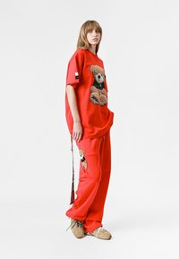 Camiseta de algodón roja, oversize, con gráfico de oso de peluche, combinada con pantalones de chándal rojos que tienen un parche de oso de peluche. Incluye zapatillas casuales.