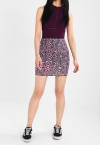 Haut sans manches ajusté de couleur violet profond associé à une jupe jusqu'au genou à motifs géométriques en rose et bleu. Porté avec des baskets noires.