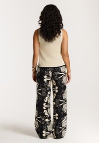 Bežs adīts topiņš kopā ar melniem platām biksēm, kurām ir krēmkrāsas akvātiskā tēma ar jūras zirgiem un čaumalām.