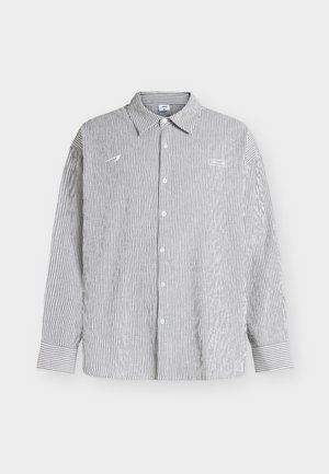 Pika varrukaga nööpidega särk, millel on vertikaalsed õhukesed mustad ja valged triibud, terava krae ja nööpidega mansetid, näidatud taustal helel pinnal.