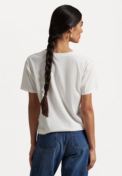 Tricou alb din bumbac cu mâneci scurte și croială lejeră, văzut din spate, combinat cu blugi albaștri din denim. Textură netedă, stil casual.