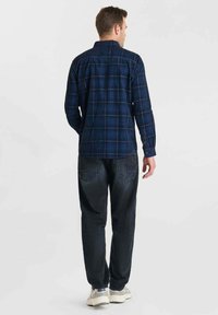 Marine geruit flanellen shirt met lange mouwen, knoopsluitingen bij de mouwen en een ronde zoom, gecombineerd met donkere denim jeans en sneakers.