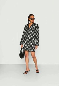 Vestido camisa em padrão preto e branco com mangas longas, decote em v e um corte relaxado. Estilizado com acessórios pretos e sandálias com tiras.