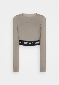 Top corto a maniche lunghe beige, con un elastico nero che mostra il logo Nike. Texture liscia e design aderente.