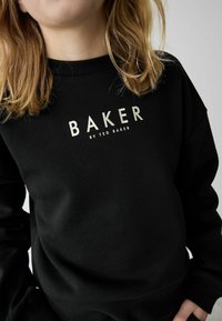 Sort sweatshirt med ribbede manchetter og halsudskæring. Har et fremtrædende guldtrykt logo "BAKER by TED BAKER" på forsiden. Blød tekstur.