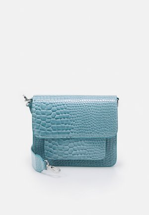 Bolso azul con textura de cocodrilo, solapa frontal y correa desmontable sobre un fondo blanco liso.