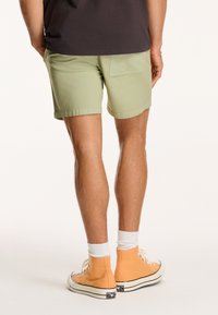 Lysgrønne shorts med en baglomme, parret med orange høj-top sneakers og hvide ankelsokker, vist fra bagenden.