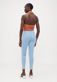 Rust halterneck top med ribbet tekstur, kombinert med lyseblå høytlivde skinny jeans. Modellen har på seg svarte og hvite blokkhæl sandaler.
