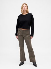 Haut noir court à manches longues associé à un pantalon évasé vert olive. Le pantalon présente des poches avant et une texture de tissu robuste. Bottines noires.