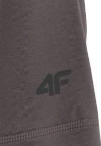 Gros plan d'un tissu gris foncé avec un logo noir "4F" imprimé près d'une couture cousue, montrant la texture et les détails du tissu.