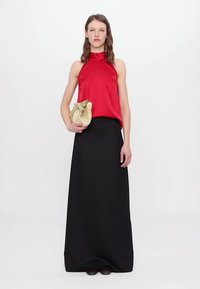 Haut halter en satin rouge associé à une jupe noire longue. Tenant une pochette dorée texturée avec un détail de nœud.