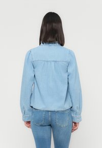 Light blue denim jacket with a rounded collar, gathered back detailing, and long sleeves. Pair with matching light blue jeans.