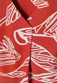 Tessuto rosso con un audace motivo astratto a onde bianche, design a V e una consistenza liscia e leggera.