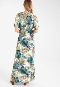 Robe maxi en tissu léger avec un imprimé de feuilles tropicales en teal, or et vert. Manches courtes et amples ; détail de taille cintrée.