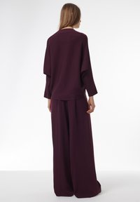 Haut à manches longues bordeaux et pantalon à taille large en tissu doux, affichant une coupe décontractée avec des coutures minimales et une texture lisse.