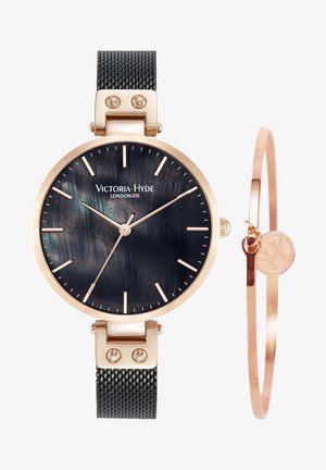 Crni remen za sat od mrežaste tkanine s okruglim kućištem zlatne boje, mračnim teksturiranim brojčanikom i akcentima u ružičastom zlatnom tonu. Uz to dolazi tanak narukvica od ružičastog zlata.