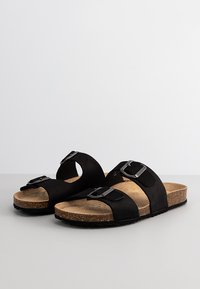 Sandales noires à glissière avec deux sangles réglables, boucles en argent, semelle en liège et semelle en caoutchouc texturée. Matière supérieure douce ressemblant à du suédé.