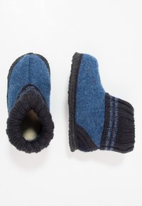 Chaussons en laine bleu et noir, avec un revers tricoté et un corps en feutre texturé, offrant un ajustement confortable et un contour de semelle contrastant.