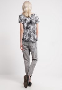 Top de manga corta con estampado en blanco y negro combinado con jeans ajustados grises, que presentan una cinturilla ligeramente elástica, y zapatos negros.