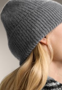 Blondyn noszący szary, prążkowany beanie i wzorzysty strój, zwrócony w prawo z widocznym uchem i kosmykami włosów.