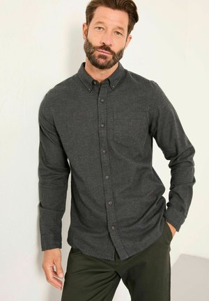 Dunkelgraues Hemd aus strukturiertem Stoff, mit Brusttasche, langen Ärmeln und Kragen. Getragen mit grünen Slim-Fit-Hosen.