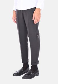 Pantaloni neri su misura con una vestibilità slim, caratterizzati da una texture liscia, orli arrotolati e tasche laterali, abbinati a mocassini neri.