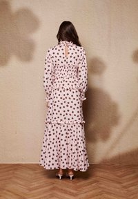 Μακριά ροζ φορεσιά με καφέ πουά, στρωτό σχέδιο, ζώνη με κουμπώματα, μακριά μανίκια και διακοσμητικές πιέτες. Διαθέτει άνοιγμα στην πλάτη σε σχήμα κλειδιού.