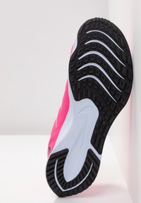 Zapatilla deportiva rosa con parte superior de malla texturizada, suela de goma negra y patrones de relieve pronunciados para tracción, que cuenta con una mediasuela blanca.