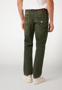 Žalia džinsinė kelnė su tiesiu siluetu, su pleistro forma atvartais ant nugaros kišenių, baltomis siūlėmis ir kontrastinga odine juosmens etiketė.