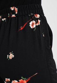 Pantalons à motif floral noir avec une taille froncée, ornés de fleurs roses et blanches et d'accents verts sur un tissu doux.