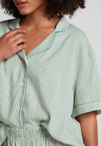 Groen-wit gestreepte button-down shirt met kraag, korte mouwen en zachte textuur. Losse pasvorm met zichtbare knoopdetails.