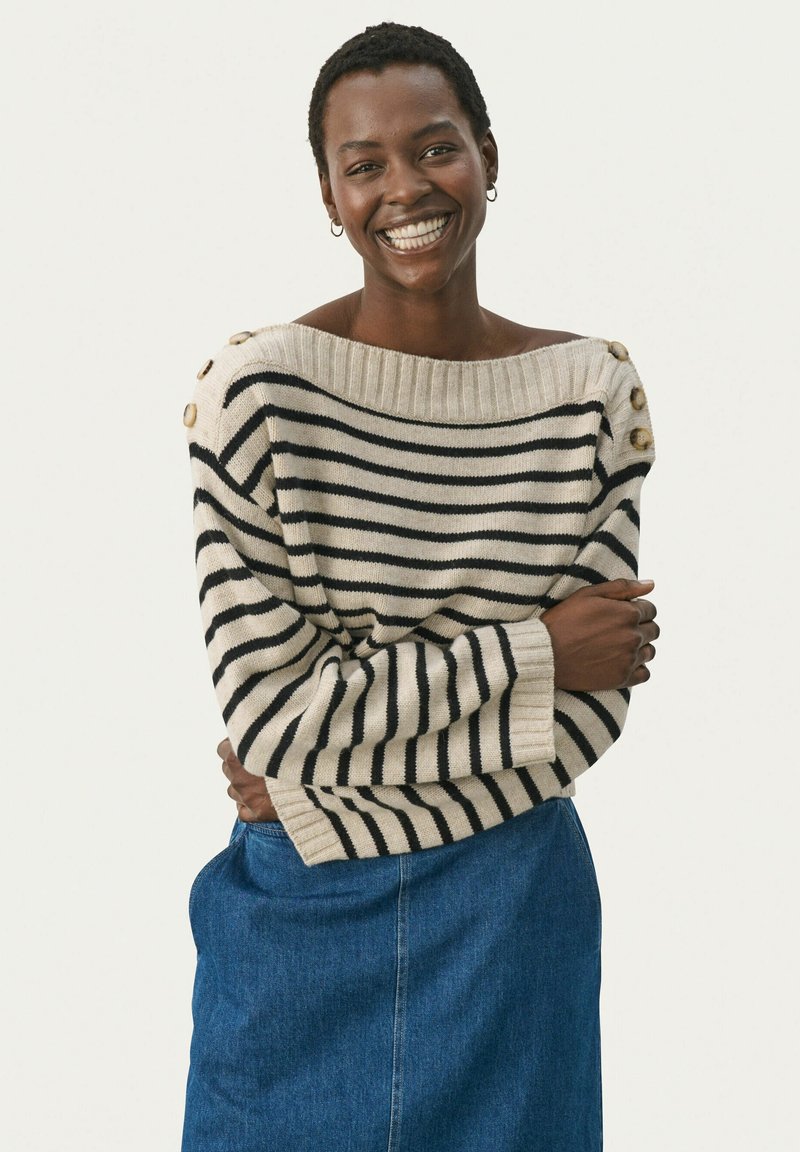 Pull rayé en beige clair et noir, présentant un design décolleté, des accents de boutons sur l'épaule et des poignets côtelés.