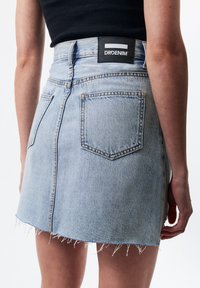 Vaaleansinisestä denimpien mini-hameesta, jossa on rispaantunut helma, takataskut ja musta brändilogo vyötäröllä.