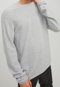 Pull gris clair en maille à manches longues avec col rond et coupe décontractée. Présente des poignets retroussés et un tissu texturé.