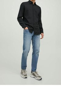 Svart knäppt skjorta, ljusblå jeans och grå sneakers. Avslappnad outfit med en figursydd design och klassiska material.