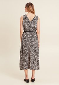 Leopardenmuster Midi-Kleid mit V-Ausschnitt, tailliertem Bund und strukturiertem Stoff. Der schwarze Gürtel betont die Taille; das Kleid hat einen fließenden Rock und ärmelloses Design.