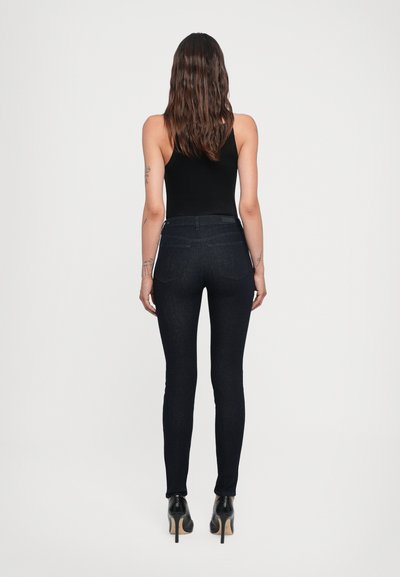 Schmale dunkelblaue Jeans aus Denim mit glatter Textur und Fünf-Taschen-Design, kombiniert mit schwarzen High-Heels und einem enganliegenden schwarzen Oberteil.