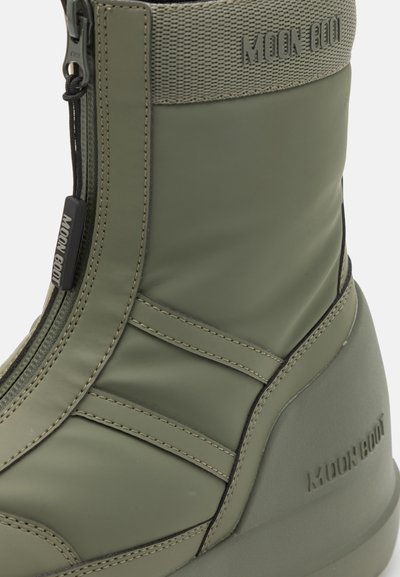 Botte imperméable verte avec une tige texturée et extensible, fermeture éclair et marquage. Équipe d'une semelle épaisse et de détails en point de croix.