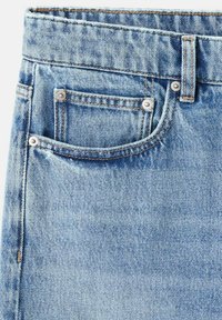 Detalle de jeans de mezclilla azul claro mostrando el bolsillo delantero derecho, el pequeño bolsillo para monedas, la presilla para el cinturón y remaches metálicos con costuras naranjas.