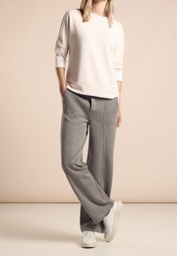 Světle růžová mikina s tříčtvrtečními rukávy v kombinaci se širokými kalhotami s šedým kostkovaným vzorem a bílými teniskami, vystavená na neutrálním pozadí.